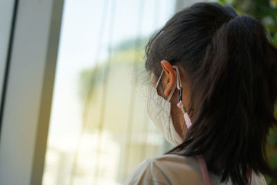 Back of asian kid she looking at the outside of glass and protection life by using mask from virus 