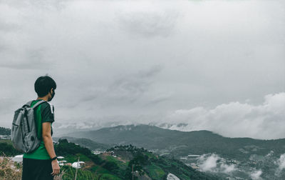 Rear view of man standing on mountain against sky