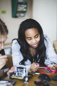 Confident female student making toy car with friend on desk in classroom at high school