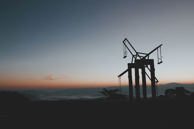 Silhouette swing on land against sky during sunset