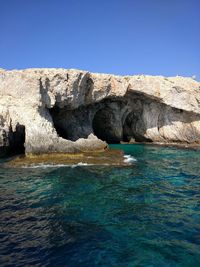 Rock formations by sea against clear blue sky