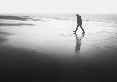 Man walking on wet shore