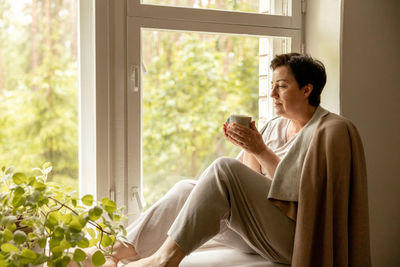 Young woman looking through window at home