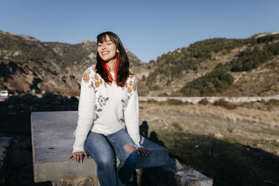 Smiling young woman standing on mountain against sky