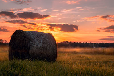 Hay bale on field against sky during sunset