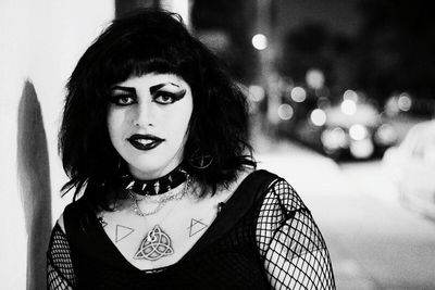 Portrait of punk woman standing by wall at night