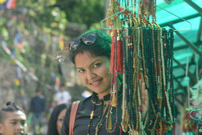 Portrait of smiling woman standing by bead necklace hanging at market stall