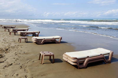 Deck chairs on beach against sky