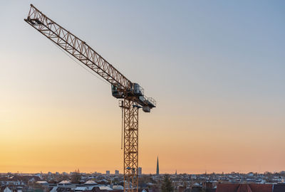 Crane at construction site against sky during sunset