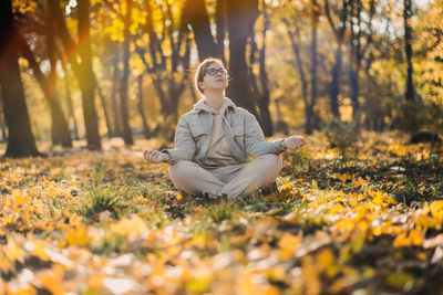 Caucasian middle aged woman meditating in lotus pose at autumn park with sunlight. yoga at fall