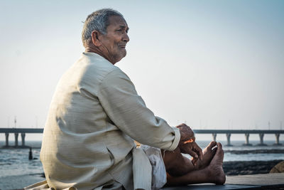 Senior man sitting on retaining wall against sea at beach