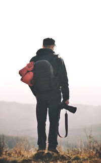 Rear view of hiker standing with camera against clear sky