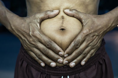 Midsection of man making heart shape on belly