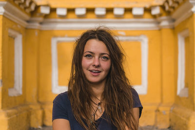 Portrait of smiling young woman standing against yellow wall