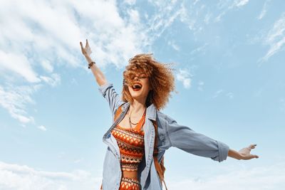 Low angle view of young woman standing against sky