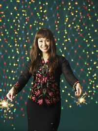 Portrait of woman with burning sparklers against illuminated lights