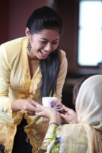 Cheerful daughter giving coffee to mother at home