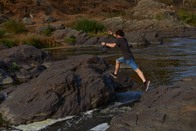 Side view of boy on rock at stream