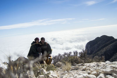 Couple sitting on rock against cloudscape