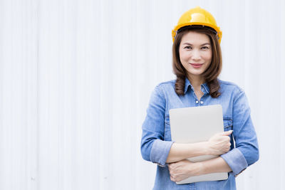 Portrait of a smiling young woman standing against wall