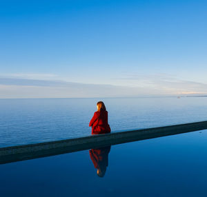 Rear view of woman sitting by infinity pool against sea