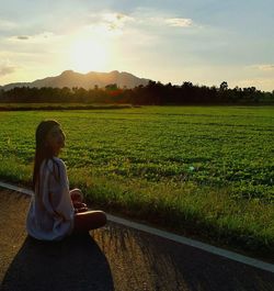 Side view portrait of woman sitting on road by farm