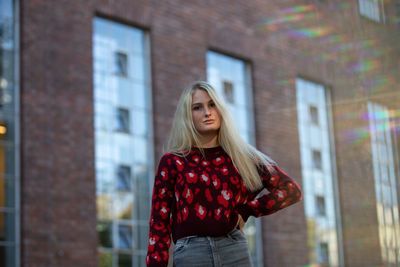 Portrait of young woman standing against red building