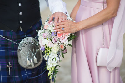 Midsection of bride and bridegroom with bouquet