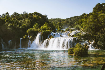 Scenic view of waterfall in forest against clear sky