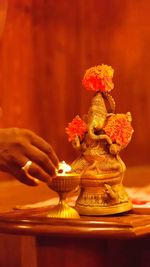 Cropped hand igniting diya by ganesha statue on table