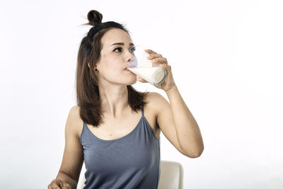 Young woman drinking drink against white background
