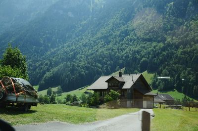 Houses by road amidst trees and buildings against mountains