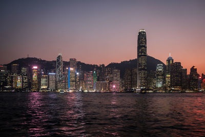 Illuminated buildings by river against sky at night