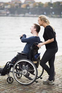 Happy disabled man with caretaker enjoying view by lake