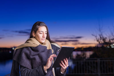 Young woman using digital tablet at dusk