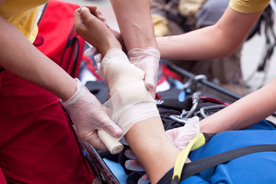 Midsection of paramedic wrapping bandage on woman hand