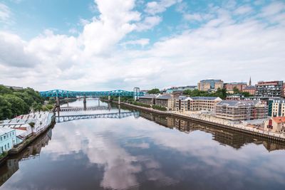 Bridge over river amidst buildings in city against sky