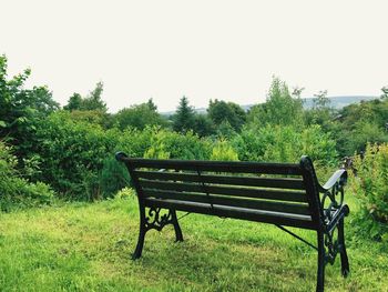 Empty bench on field against clear sky