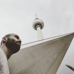 Low angle view of thoughtful man standing by fernsehturm against sky