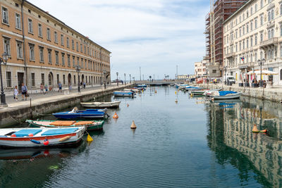 Boats moored on canal amidst buildings in city against sky