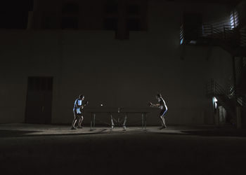 Friends playing table tennis against building at night