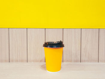 Close-up of yellow cup on table against wall