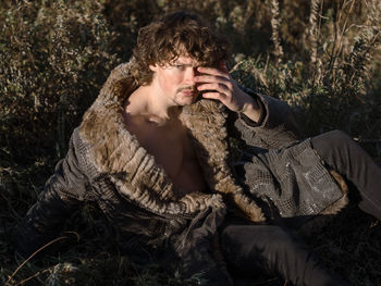 Young man looking away while sitting on land