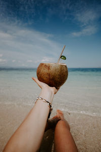 Cropped hand of woman holding coconut at beach