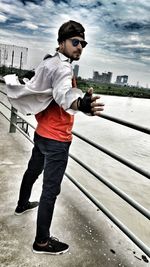 Side view of young man standing by railing against sky