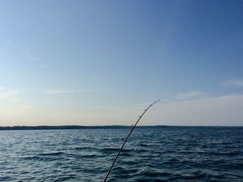 Fishing rod over sea against blue sky