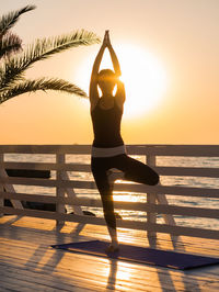 Full length of woman doing yoga on promenade against sky during sunrise