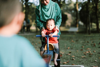 Mother holding son sitting on seesaw at playground