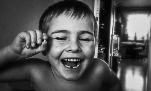 Close-up portrait of laughing shirtless boy who holds his teeth in camera