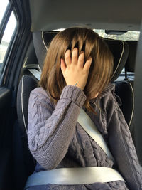 Girl wearing warm clothing and seat belt while sitting in car